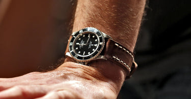 rolex submariner watch on a wrist and brown vintage ammo pouch strap