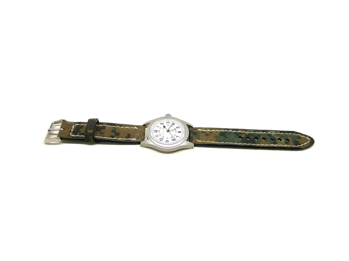 Fission watch strap in green and brown with a camouflage pattern and cream edge stitching, shown fitted to a watch.