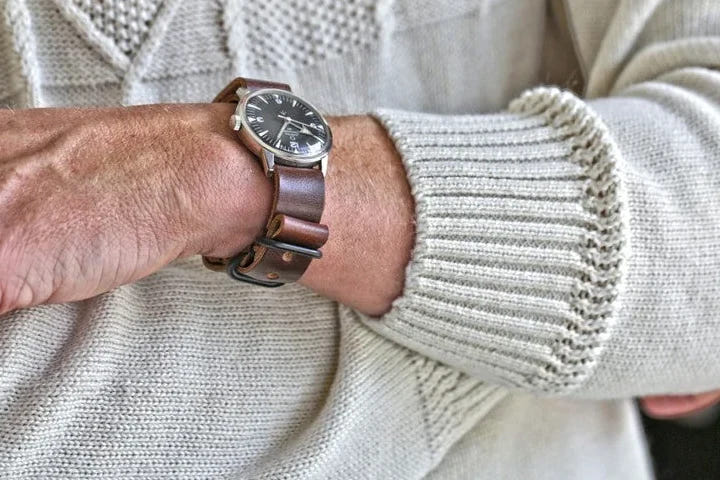 Brown leather single-piece watch strap worn with a cream cable-knit sweater