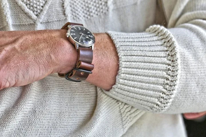Brown leather single-piece watch strap worn with a cream cable-knit sweater